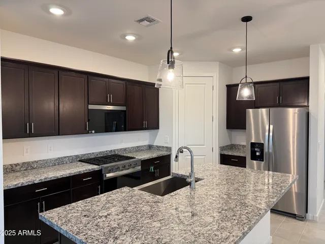 a kitchen with stainless steel appliances granite countertop wooden cabinets a stove a sink a refrigerator and a wooden cabinets