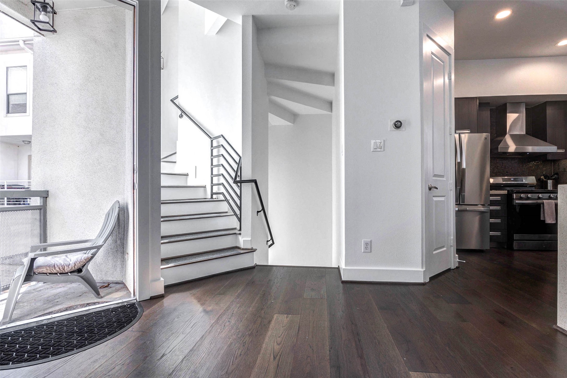 5715 Larkin Street, Unit D Houston, TX 77007 - Photo 12 of 38 View highlighting the staircase with sleek metal railing leading to upper levels, adding architectural interest and vertical flow. The adjacent entry door with glass insert allows natural light into the space. Clean white walls and dark flooring create a striking contrast that enhances the contemporary feel.