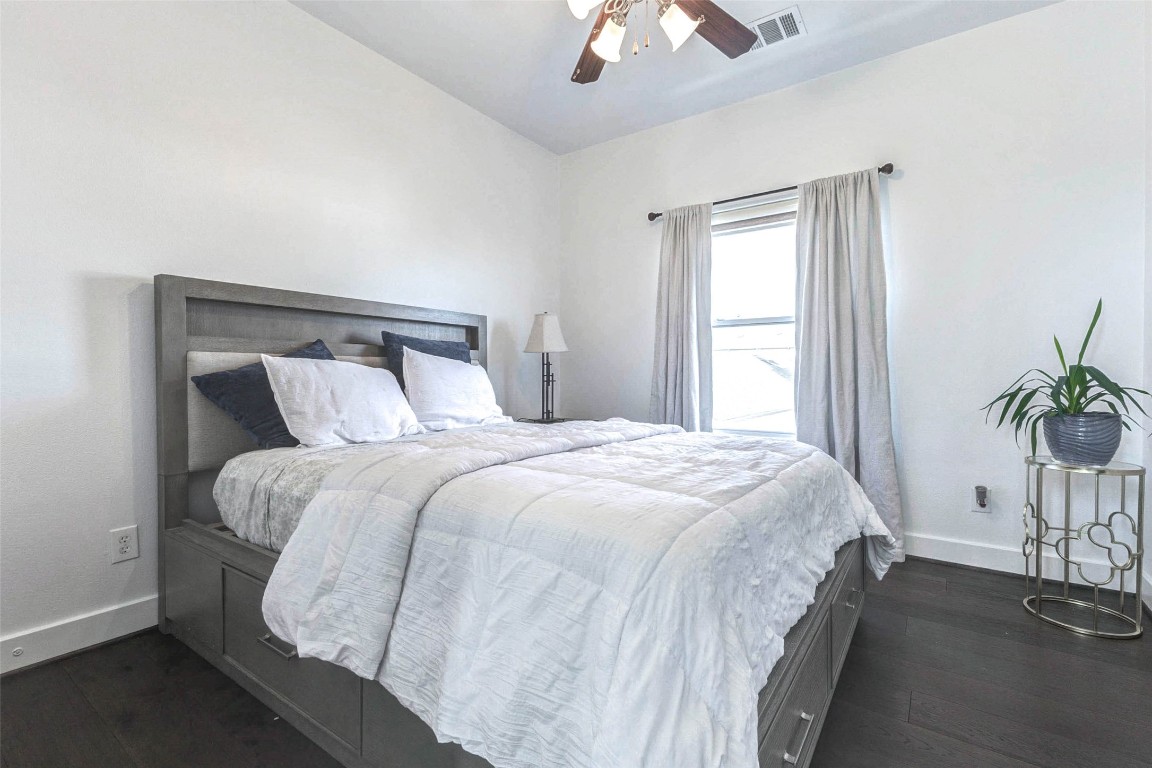 5715 Larkin Street, Unit D Houston, TX 77007 - Photo 21 of 38 Spacious bedroom featuring rich dark hardwood floors that contrast beautifully with light walls and bedding. A large window allows natural light to fill the room, while ceiling fan and overhead lighting provide comfort year-round. The room offers generous proportions for a complete, restful retreat.