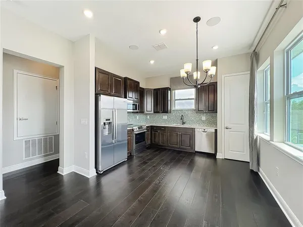 a large white kitchen with a refrigerator a sink dishwasher a stove and a dining table with wooden floor