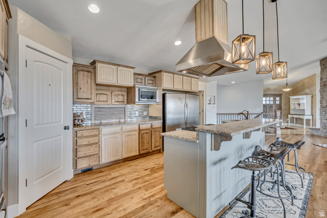 3054 West Ridgeline Road Stockton, UT 84071 - Photo 37 of 88 Kitchen with light wood-style flooring, a kitchen bar, light stone countertops, decorative light fixtures, and island range hood