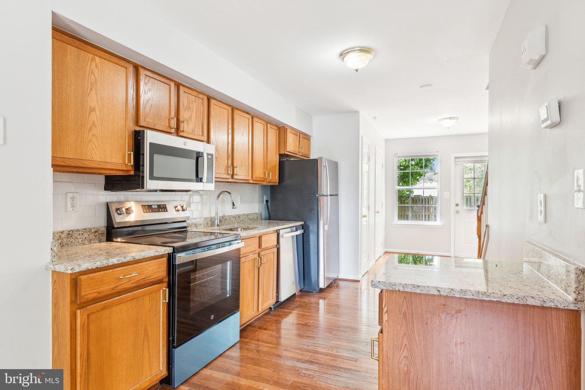 a kitchen with stainless steel appliances granite countertop wooden cabinets a stove top oven a sink and dishwasher with wooden floor