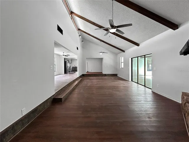 an empty room with wooden floor ceiling fan and windows