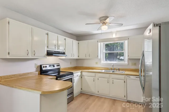 a kitchen with a sink dishwasher and white cabinets with wooden floor