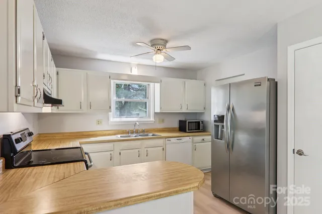 a kitchen with stainless steel appliances granite countertop a refrigerator a sink a stove and white cabinets