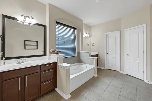 a spacious en suite bathroom with a double vanity sink a large mirror and a bathtub