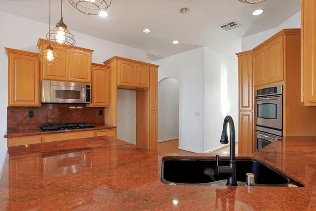 a kitchen with stainless steel appliances granite countertop a sink a stove a refrigerator and island with wooden floor