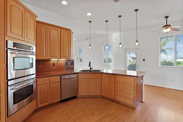 a kitchen with stainless steel appliances granite countertop a refrigerator a sink dishwasher a stove and white countertops with wooden floor