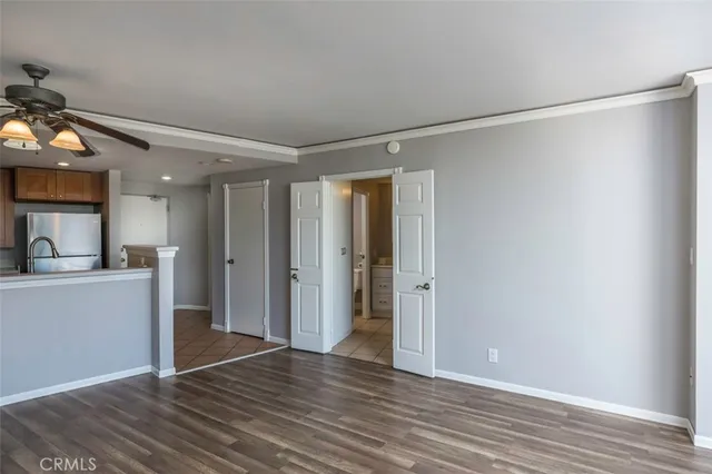 a view of an empty room with wooden floor and a kitchen