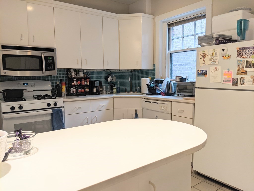 a kitchen with stainless steel appliances a sink a stove a microwave a refrigerator cabinets and a window