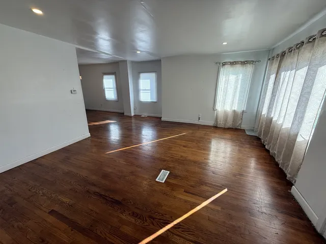 an empty room with wooden floor and windows with curtains