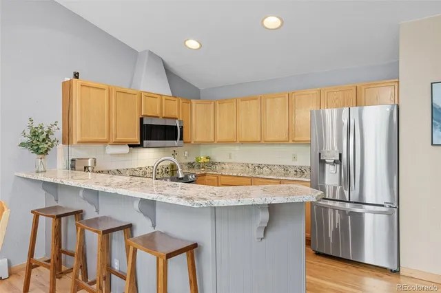 a kitchen with stainless steel appliances granite countertop a refrigerator a sink a stove and white cabinets with wooden floor