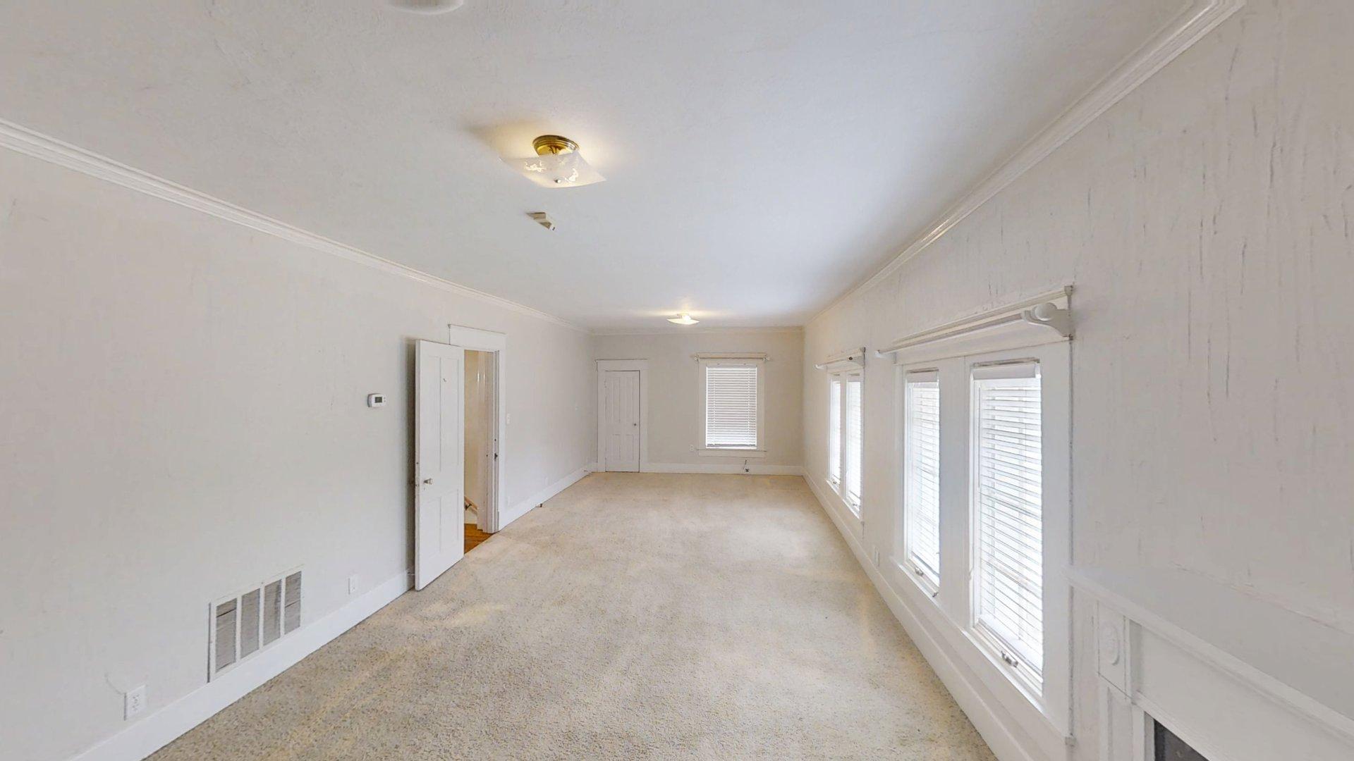 219 F Street Southwest Ardmore, OK 73401 - Photo 25 of 58 Expansive room featuring light-toned carpeting, multiple windows with blinds, crown molding, and a flush mount ceiling light