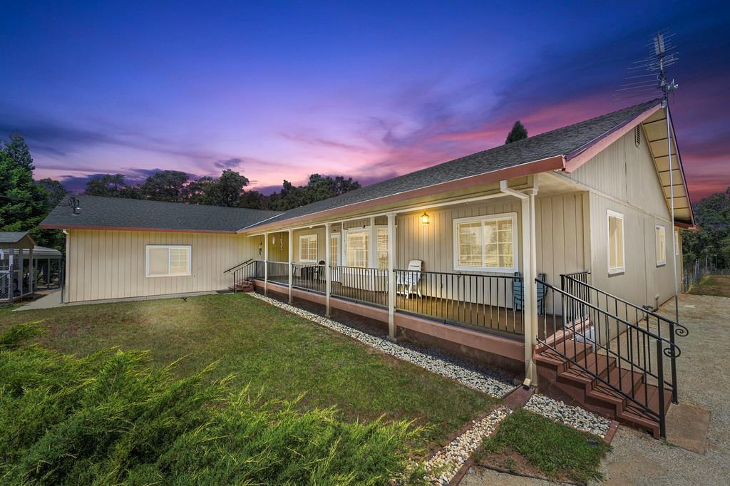 Ranch-style residence featuring a covered porch with black metal railings, a gabled roof, and a gravel driveway