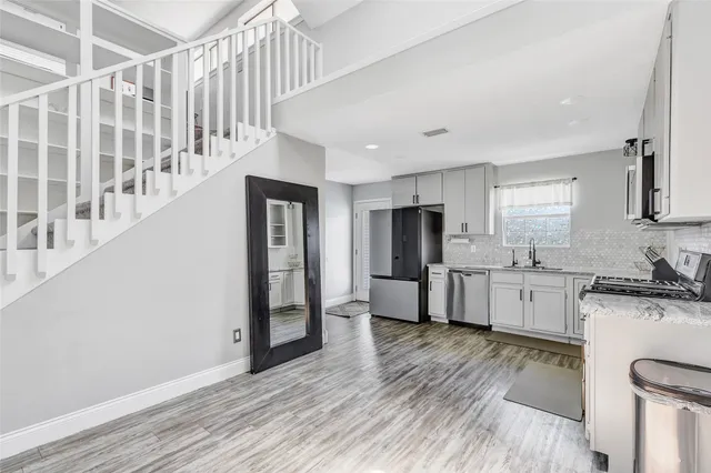 a kitchen with granite countertop a refrigerator a stove a sink and white cabinets with wooden floor