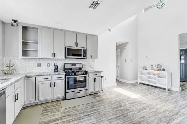 a kitchen with stainless steel appliances white cabinets a sink a stove a microwave and wooden floors