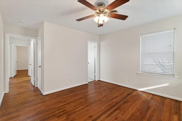 an empty room with wooden floor chandelier fan and windows