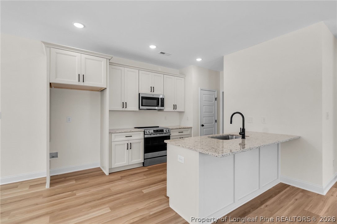 131 Merle Road Pinebluff, NC 28373 - Photo 11 of 33 a kitchen with stainless steel appliances granite countertop a sink stove refrigerator and white cabinets with wooden floor