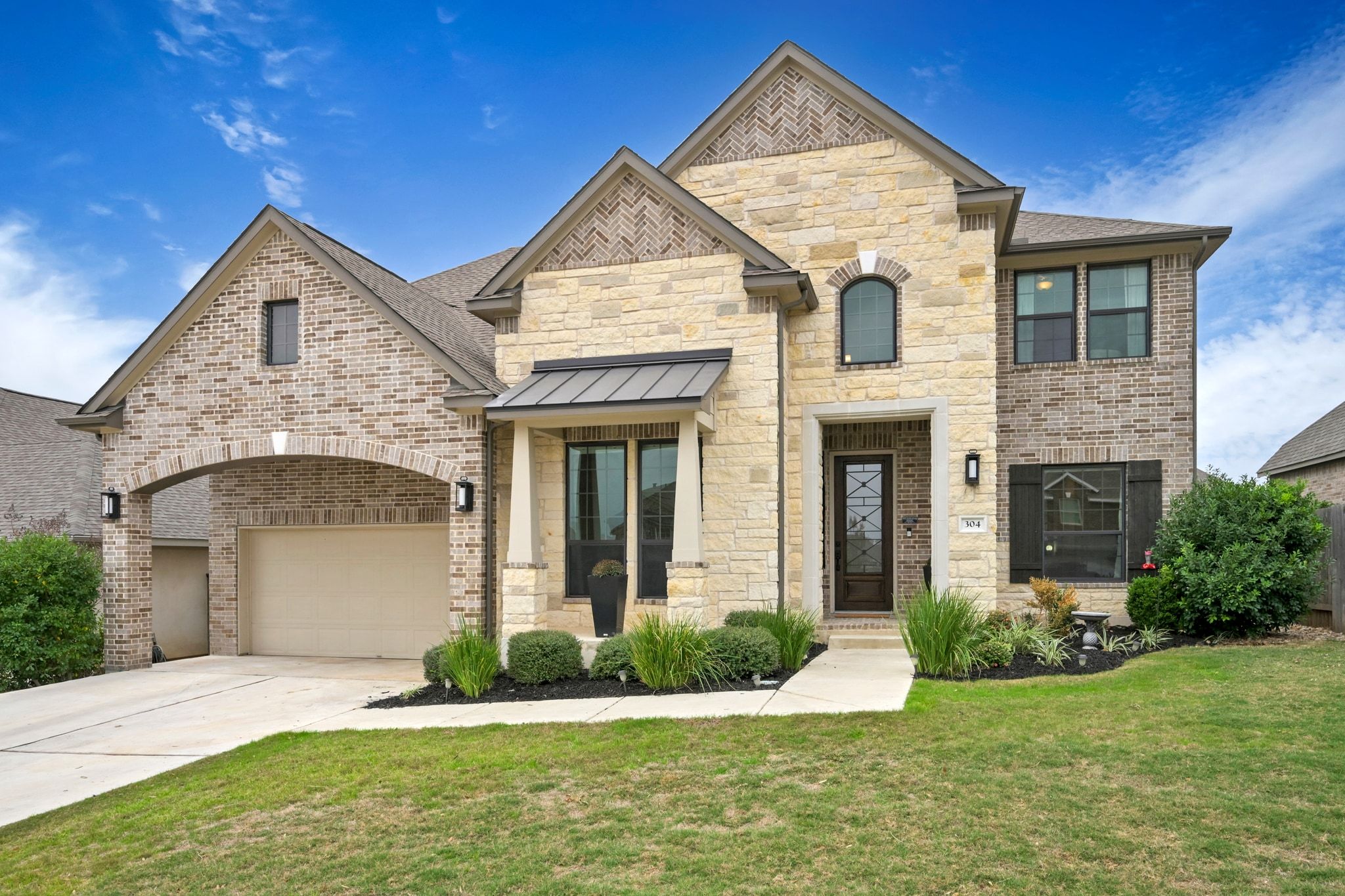 front lawn, a garage, concrete driveway, stone siding, and a standing seam roof, garage