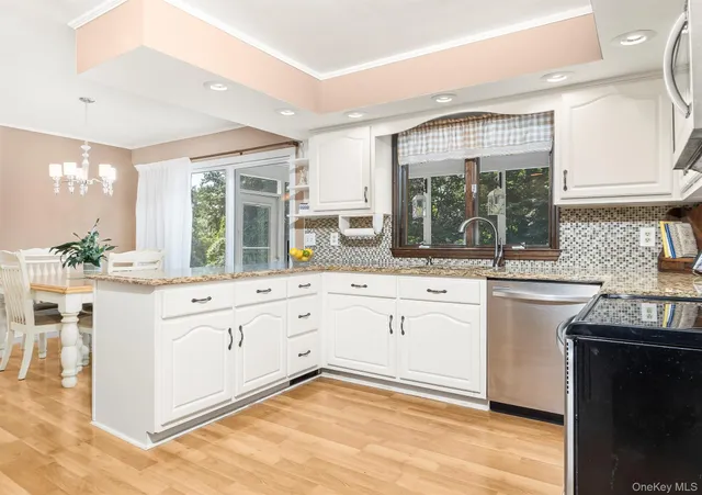 a large white kitchen with granite countertop a stove a sink a window and stainless steel appliances