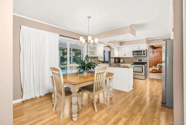 a dining room with stainless steel appliances kitchen island granite countertop a table chairs and a wooden floor