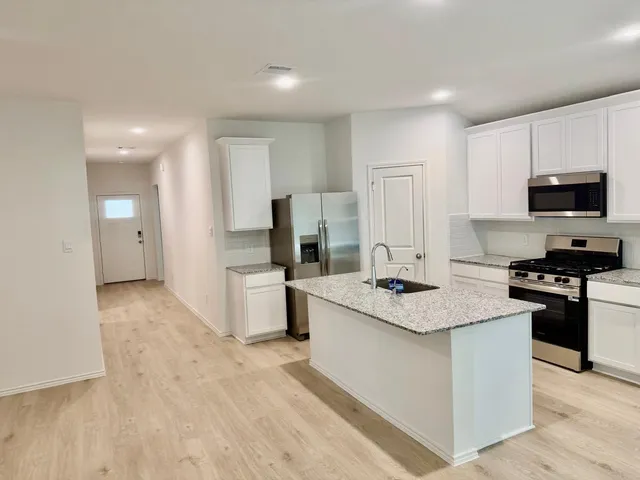 a kitchen with stainless steel appliances granite countertop a stove top oven a refrigerator a sink and dishwasher with wooden floor