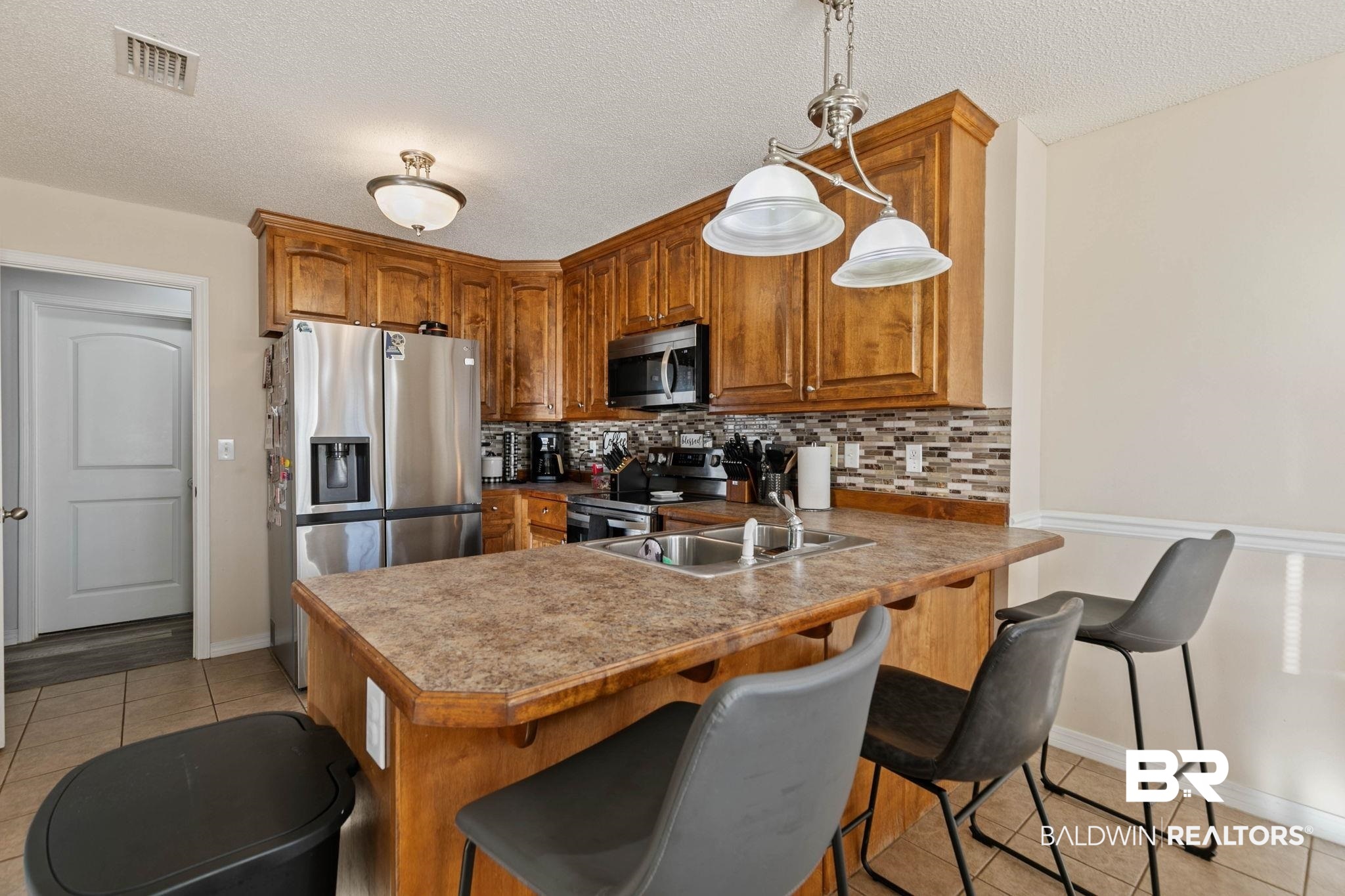 55750 Lottie Road Perdido, AL 36562 - Photo 65 of 84 Kitchen featuring wood finish cabinets, light tile patterned floors, stainless steel appliances, a breakfast bar area, and a textured ceiling