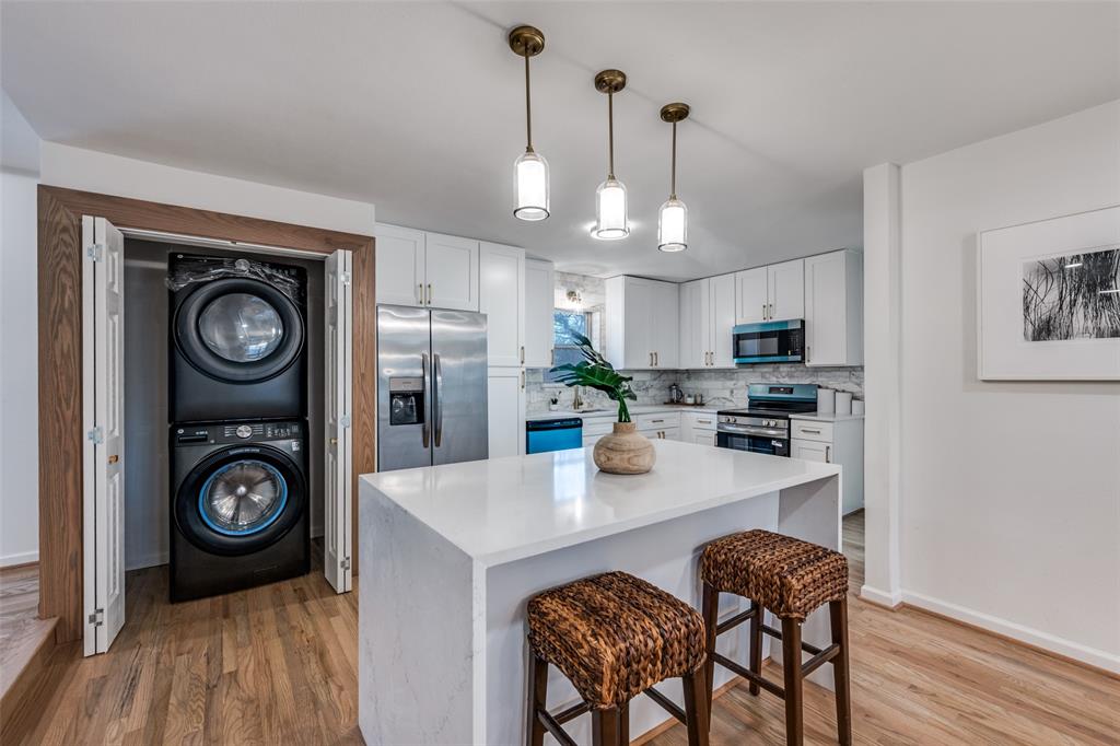 624 Forest Lane Hurst, TX 76053 - Photo 8 of 25 Kitchen featuring a kitchen breakfast bar, stainless steel appliances, pendant lighting, stacked washer and dryer, and a kitchen island