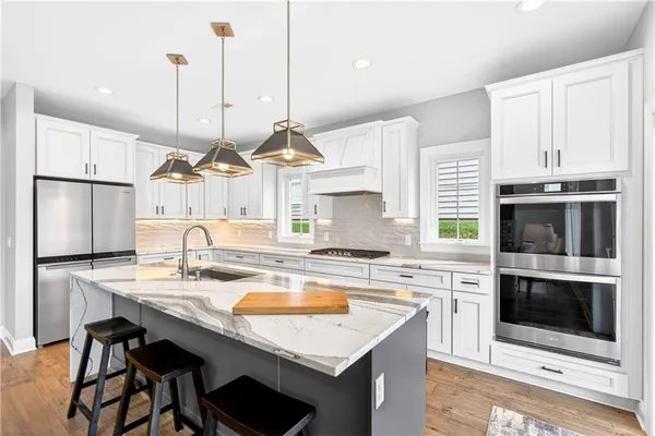 a kitchen with stainless steel appliances granite countertop a stove a sink a microwave a refrigerator a stove and white cabinets