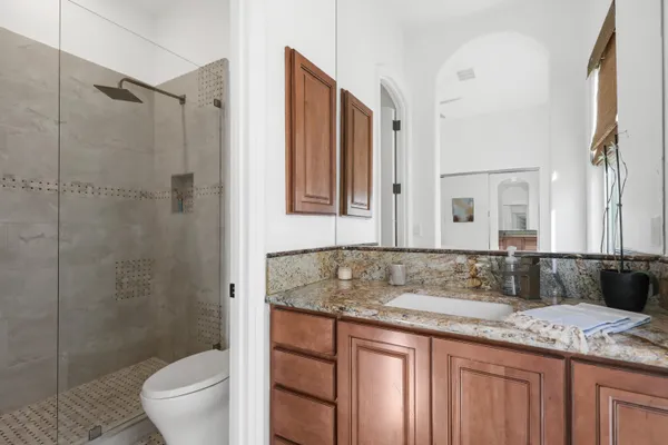 a bathroom with a granite countertop sink a toilet a mirror and shower