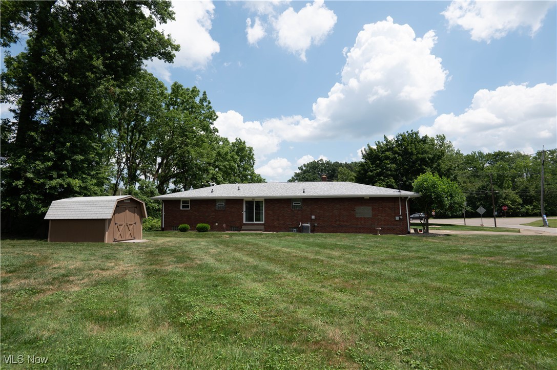 Rear view of house featuring a storage unit, brick siding, and a yard
