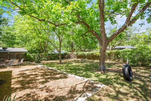 a backyard of a house with table and chairs under an large trees