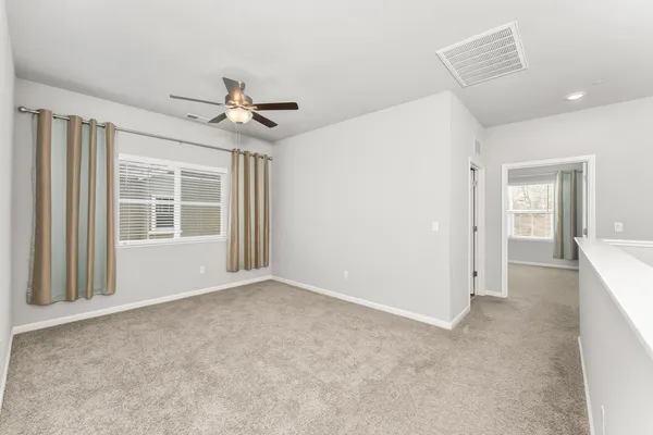 an empty room with chandelier fan and windows