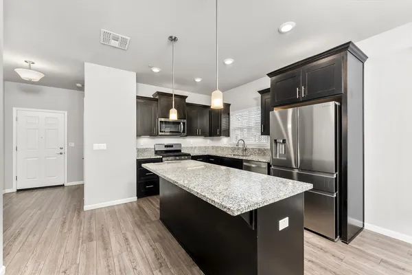 a kitchen with stainless steel appliances granite countertop a refrigerator a sink dishwasher a stove and white countertops with wooden floor