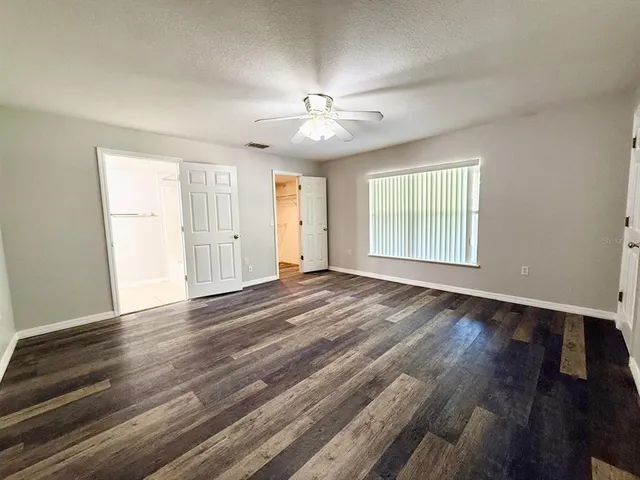 an empty room with wooden floor fan and windows