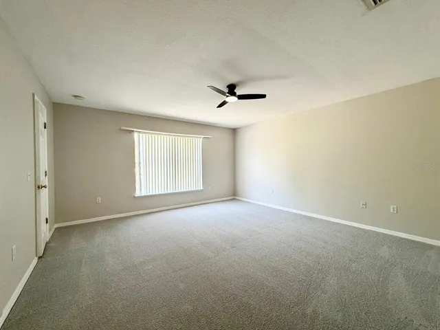 an empty room with chandelier fan and windows