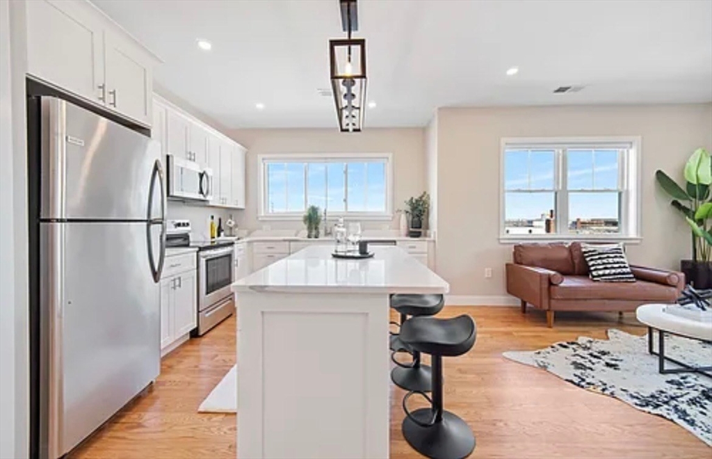 2-4 Hecla Street, Unit 1 Boston, MA 02122 - Photo 9 of 9 a kitchen with stainless steel appliances kitchen island granite countertop a refrigerator a stove a sink dishwasher a dining table and chairs with wooden floor