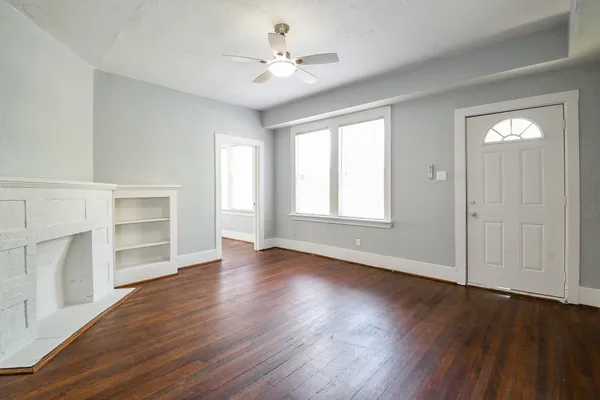 an empty room with wooden floor chandelier fan and windows