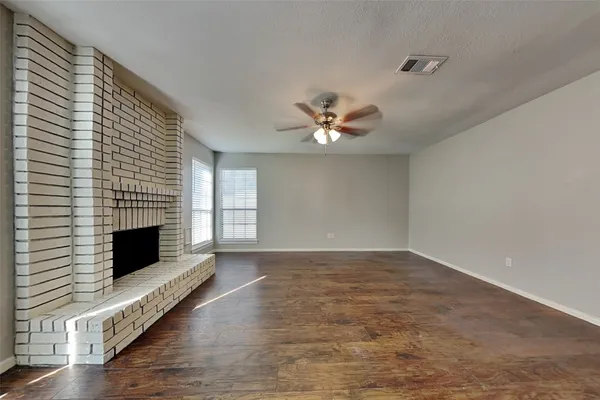 a view of an empty room with wooden floor fireplace and a window