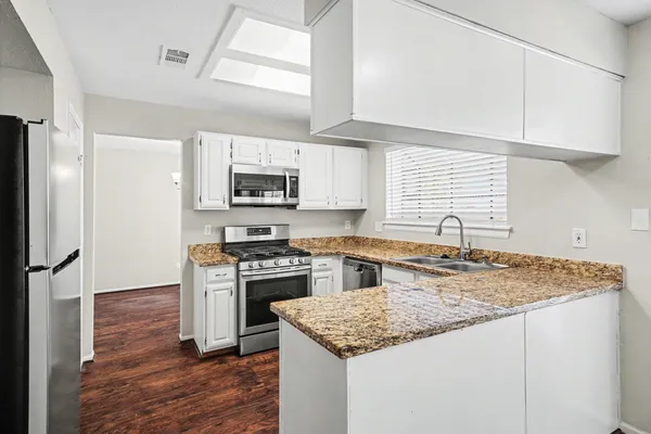 a kitchen with granite countertop a sink stainless steel appliances and white cabinets