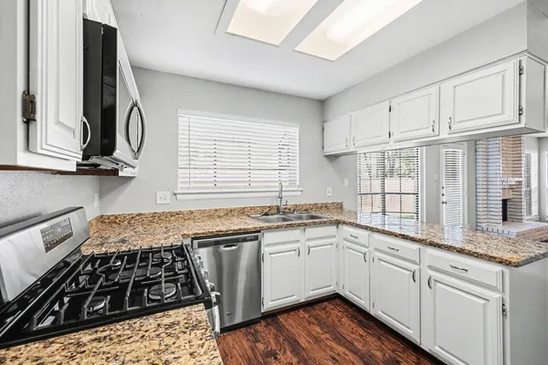 a kitchen with stainless steel appliances a sink dishwasher stove and white cabinets with wooden floor