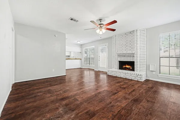 a view of an empty room with wooden floor fireplace and a window