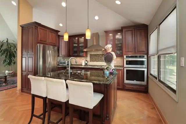 a kitchen with stainless steel appliances kitchen island granite countertop a refrigerator a stove a sink a dining table and chairs with wooden floor