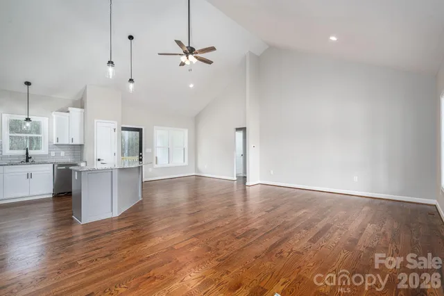 a view of an empty room and kitchen with wooden floor