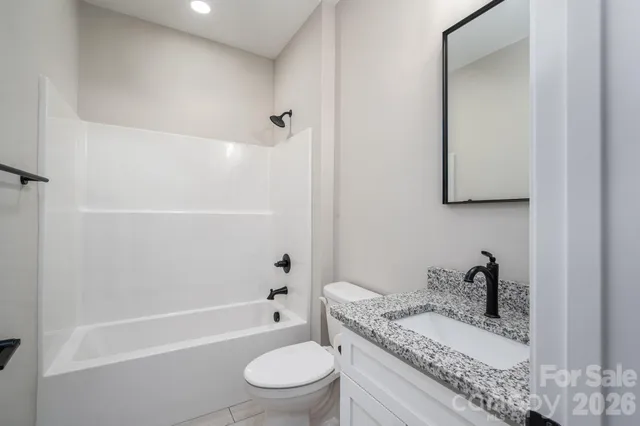 a bathroom with a granite countertop bathtub shower sink vanity mirror and toilet