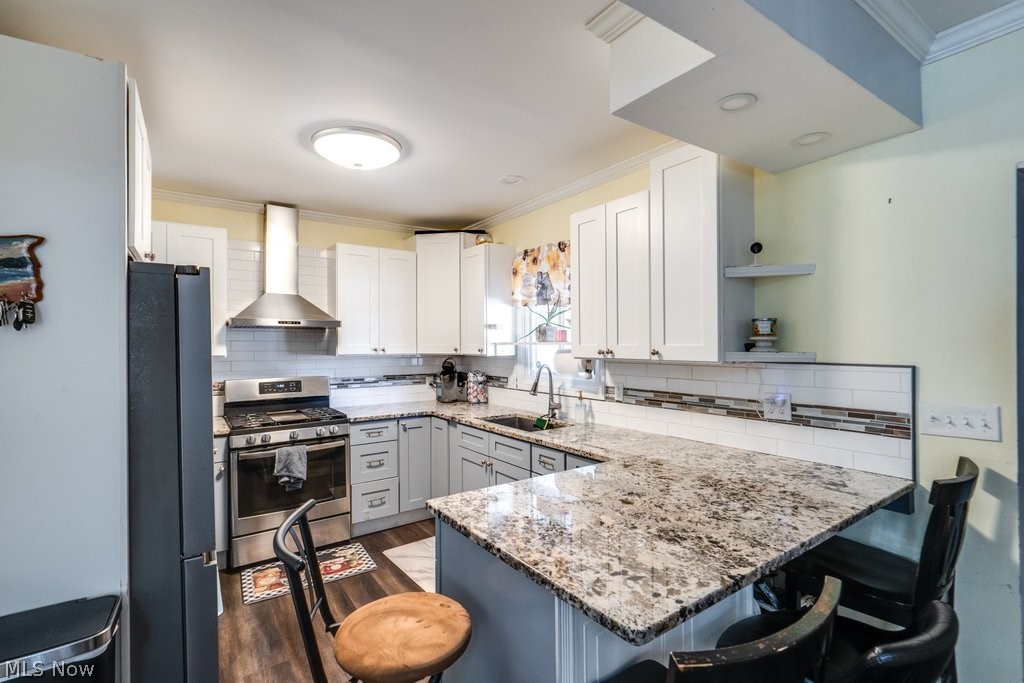 3566 Lloyd Road Cleveland, OH 44111 - Photo 13 of 31 Kitchen featuring dark hardwood / wood-style flooring, black refrigerator, wall chimney exhaust hood, stainless steel range with gas stovetop, and sink