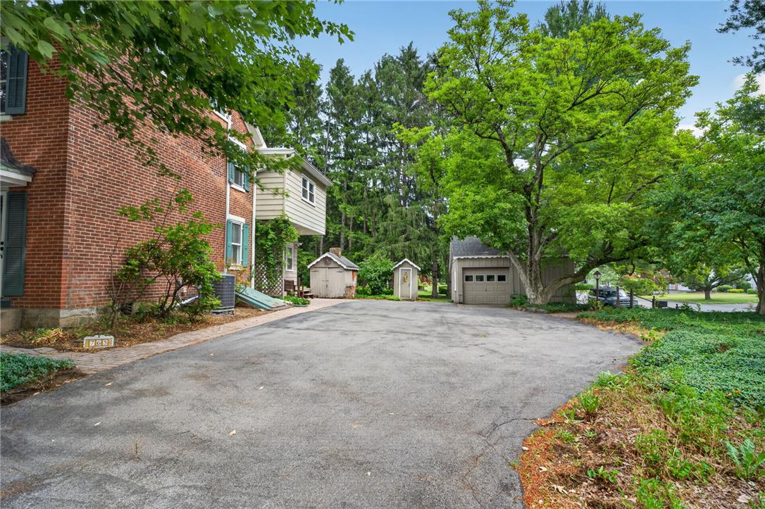 765 East Macada Road Bethlehem, PA 18017 - Photo 2 of 46 A classic brick exterior with a paved driveway leads to a detached garage, nestled amongst mature trees and greenery.