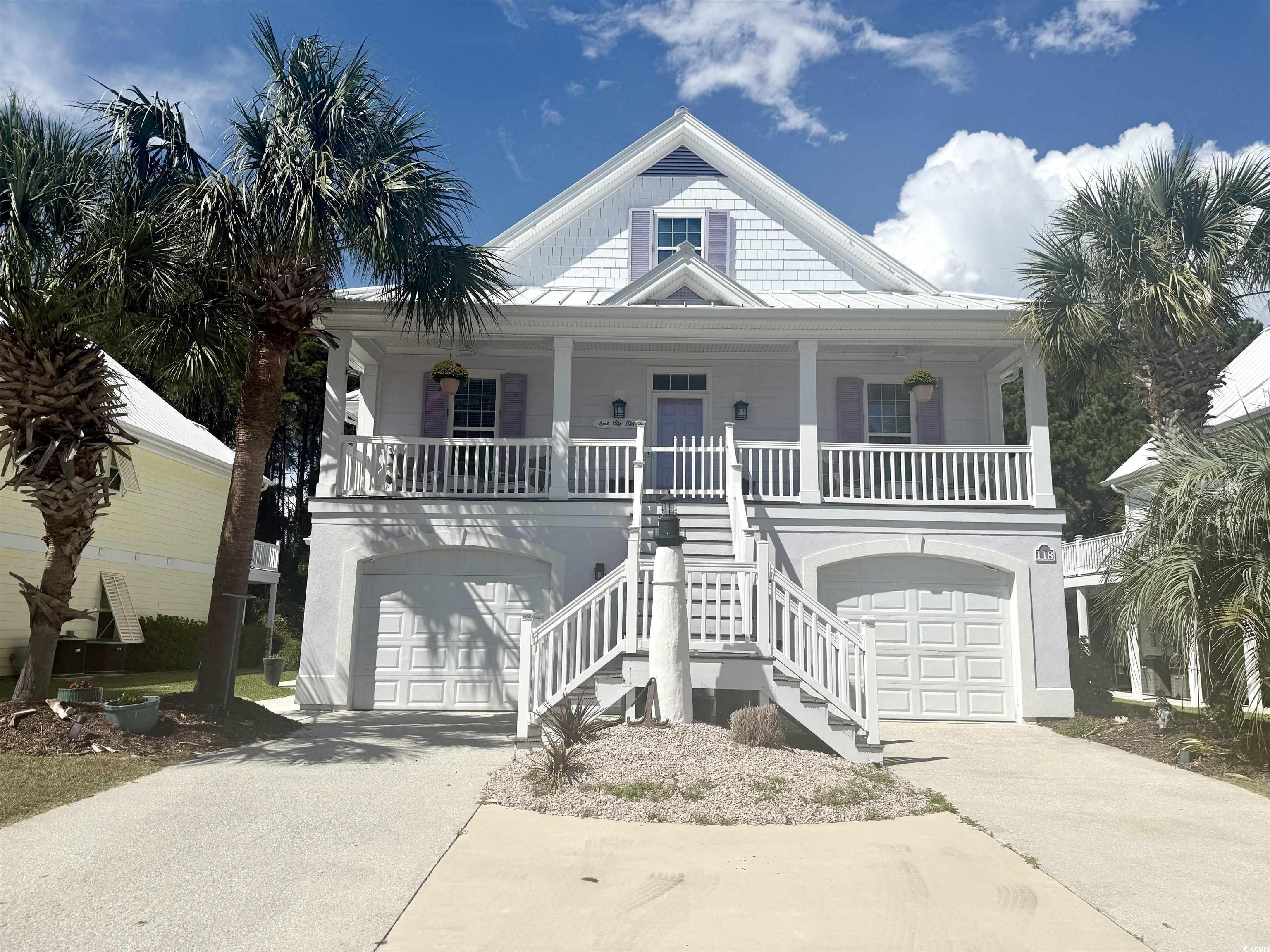 Beach home with a standing seam roof, covered porch, stairs, and driveway