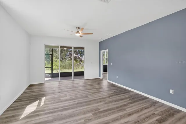 a view of an empty room with wooden floor and a ceiling fan