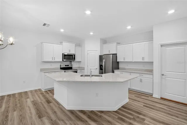 a kitchen with stainless steel appliances granite countertop a sink dishwasher a refrigerator white cabinets and wooden floor